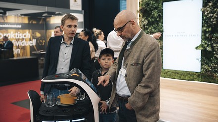 Messemitarbeiter steht vor einem Serviceroboter und tippt etwas ein Messemitarbeiter steht vor einem Serviceroboter und tippt etwas ein