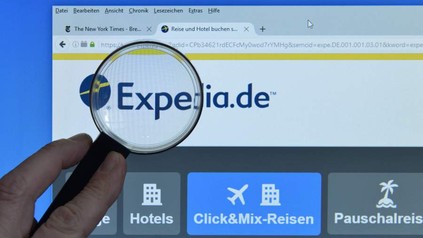 Mann hält Lupe vor Logo von Expedia.de an Bildschirm