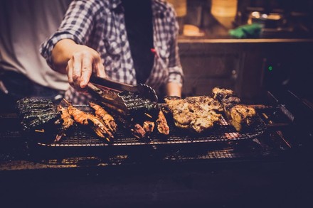 Mann an Grill hebt Fleisch mit Grillzange an