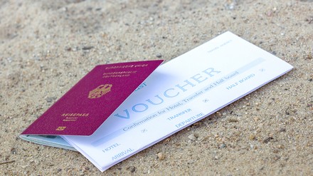 Reisegutschein und ein Reisepass liegen im Sand