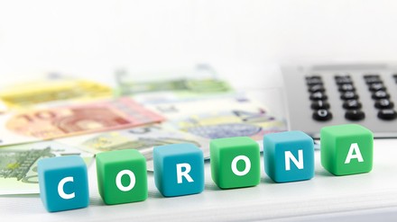 Euro-Noten, ein Taschenrechner und Buchstabenwürfel mit dem Wort „Corona“