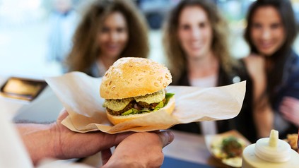 Ein Foodtrucker serviert einen Burger an drei junge Damen
