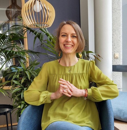 Elizabeth Buchheim sitzt auf blauem Sessel im Hintergrund eine Pflanze und eine moderne Deckenlampe aus Holz