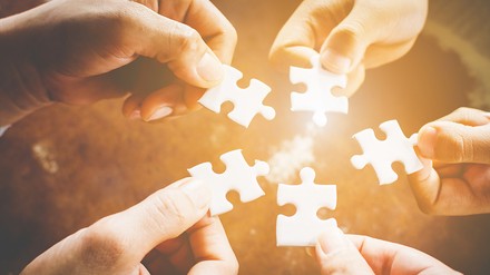 Hände von verschiedenen Menschen die Puzzelteile heben