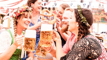 Gruppe von Freunden am Biertisch stoßen mit Maß an und lachen auf dem Oktoberfest.