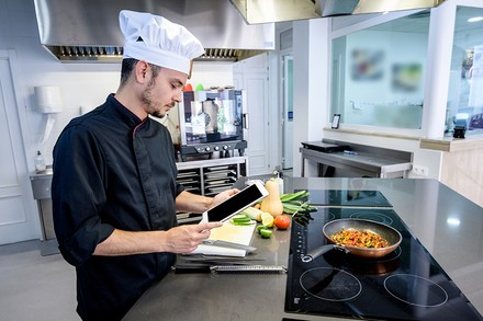 Arbeitsanweisungen per App statt direkt vom Küchenchef? Dies soll einem Gastronomieunternehmen HOW.FM zufolge bis zu 50 Prozent der Kosten ersparen. (© charlymorlock/Fotolia)
Ein Koch mit einem Handy in der Hand