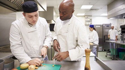 Auszubildender erklärt dem Kochazubi, was zu tun ist