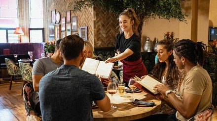 Kellnerin überreicht Speisekarten an eine Gruppe