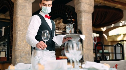 Kellner mit Mundschutz deckt einen Restauranttisch ein