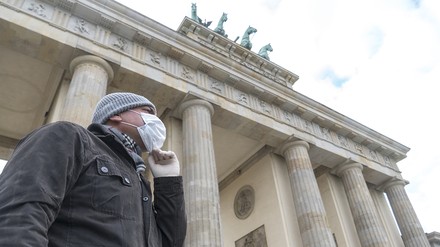 Mann mit Mundschutz vorm Brandenburger Tor in Berlin