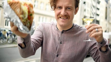 Mann mit Schnurrbart hält Döner und Rebensaft in Händen