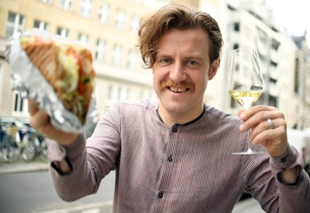 Mann mit Schnurrbart hält Döner und Rebensaft in Händen