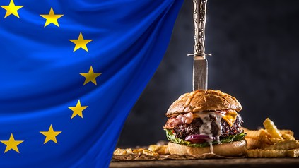 Eine EU-Flagge und ein Burger, in dem ein messer steckt