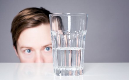 Mann schaut auf halb leeres Glas Wasser