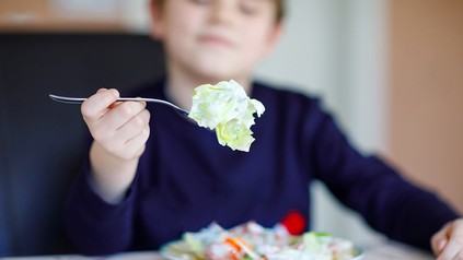 Ein Kind isst Salat in einer Kantine