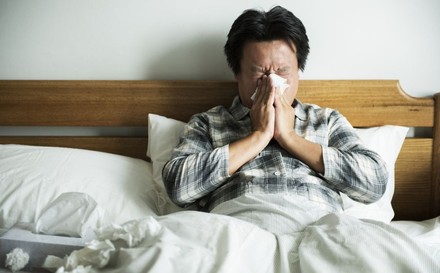 Mann liegt erkältet im Bett