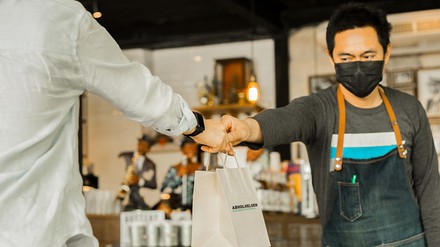 Take-away- und Lieferservice-Angebote sind für Gastronomen während des Lockdowns ein wichtiger Umsatzbringer. (Foto: ©Abholhelden.de)
Ein Mann mit Mund-Nasen-Maske gibt einem Kunden eine Papiertüte mit To-go-Speisen