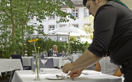 Kellnerin deckt einen Tisch in einem Gastgarten ein