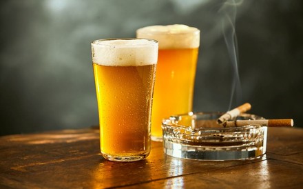 Zwei rauchende Zigaretten in einem Aschenbecher neben dem zwei Gläser Bier stehen