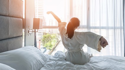 Frau streckt sich nach dem Aufwachen im Hotelbett
