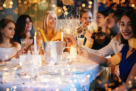 Eine Gruppe fröhlicher Menschen stößt mit Sekt gemeinsam an einem weihnachtlich gedeckten Tisch an