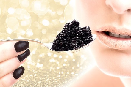 Eine Frau hält sich einen Löffel Kaviar an den Mund