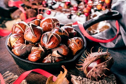 Frische Esskastanien in einer Pfanne, der Hintergrund ist weihnachtlich geschmückt
