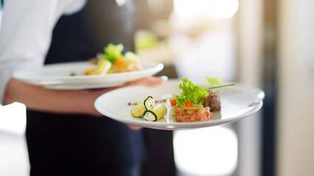 Servicekraft mit grazil angerichteten Speisen