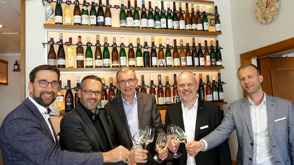 Ein Organisatorenteam stößt in einem Weinkeller mit Gläsern an.
