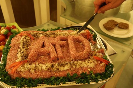 Auf einem Tablett befindet sich eine große Portion Mett aus dem das Wort AfD geformt wurde. Eine Person beginnt gerade damit das Mett anzuschneiden