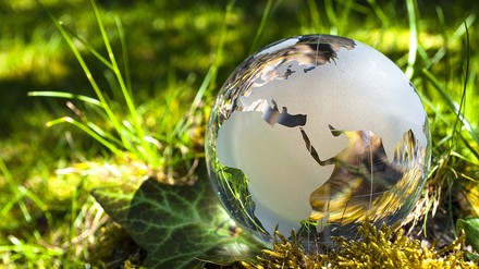 Weltkugel aus Glas in der Erde bzw. Gras mit Sonnenlicht