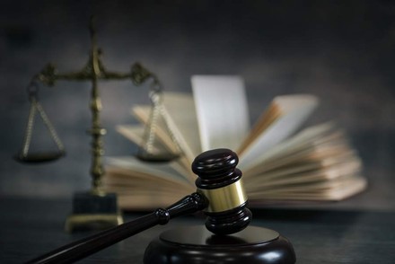 Ein Richterhammer liegt vor einem offenen Buch und einer Waagschale