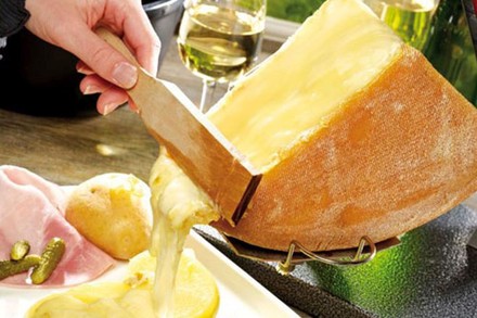 Eine Person schabt flüssigen Käse von einem großen Stück eines Käserads ab