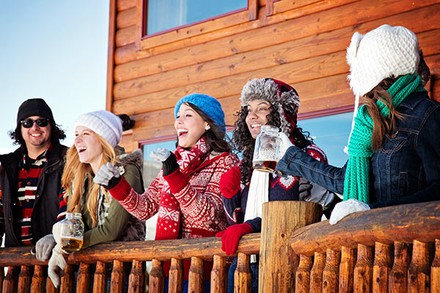 Fünf Personen stehen auf einer Terrasse einer Skihütte in Winterbekleidung und lachen