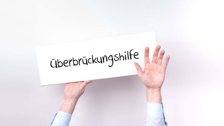 Hände halten Schild mit der Aufschrift „Überbrückungshilfe“ in die Luft