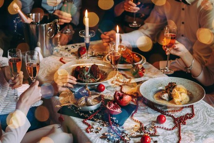 Ein weihnachtlich gedeckter Tisch an dem mehrere Personen gutes Essen verzehren und mit Sekt anstoßen