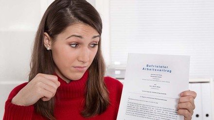 Junge Frau schaut skeptisch auf ihren befristeten Arbeitsvertrag