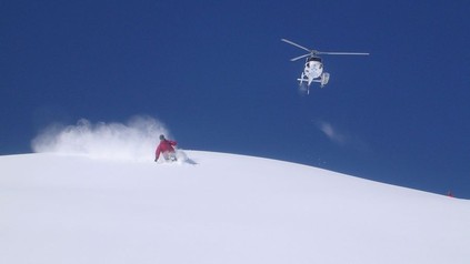 Ein Mann beim Skifahren und ein Helikopter im Hintergrund
