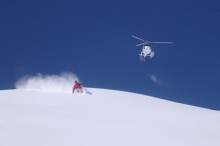 Ein Mann beim Skifahren und ein Helikopter im Hintergrund