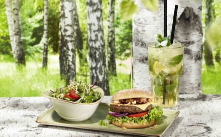 Burger fast wie in freier Natur lassen sich bei „Hans im Glück“ genießen – jetzt auch in der Schweiz. (© Hans im Glück)
Eine Portion Burger und Salat mit einem frischen Getränk im Restaurant Hans im Glück. Im Hintergrund sieht man Birkenbäume