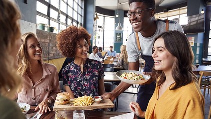 Servicekraft bringt Teller mit Burgern an den Tisch