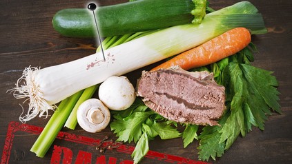 Ein Zucchini, ein Lauch in dem eine Nadel steckt, Pilze, eine Karotte und ein Stück Fleisch auf Kräutern, darunter ein Stempel auf dem Danger steht