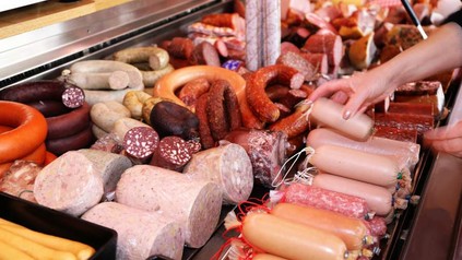 Eine Fleischwarentheke, die von einer Metzgereifachverkäuferin befüllt wird