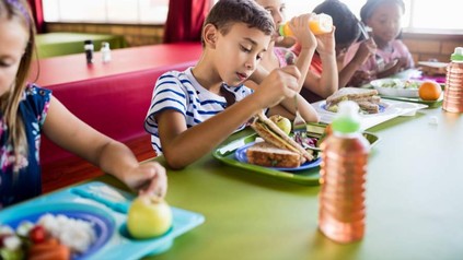Eine Gruppe Schüler am Tisch beim Verzehr des Mittagsessens aus der Schulkantine