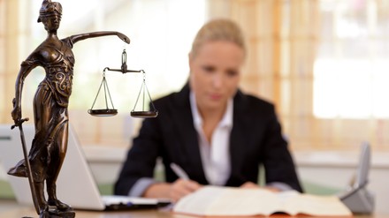 Frau im Hintergrund arbeitet, im Vordergrund steht eine Statue der Justitia