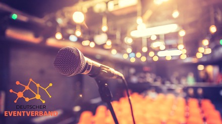 Leerer Veranstaltungsraum mit Mikrofon im Vordergrund, Hintergrund mit Sitzreihen verschwommen