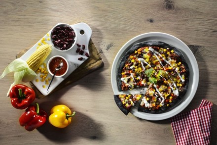 Eine Pizza aus schwarzem Teig mit Mais, Paprika und Kidney-Bohnen belegt, daneben die Zutaten des Belages