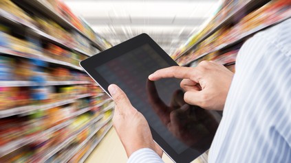 Mann mit Touchpad zwischen Lebensmittelregalen im Supermarkt