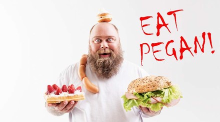 Ein bärtiger Mann hät eine belegte Semmel und eine Waffel mit Sahne und Erdbeeren in den Händen. Um seine Schulter liegt eine Wurstkette und auf seinem Kopf liegt ein Krapfen. An der Seite steht EAT PEGAN