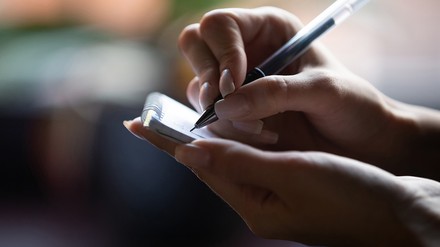 Nahaufnahme von Händen einer jungen Frau, die gerade etwas auf einen Notizblock schreibt